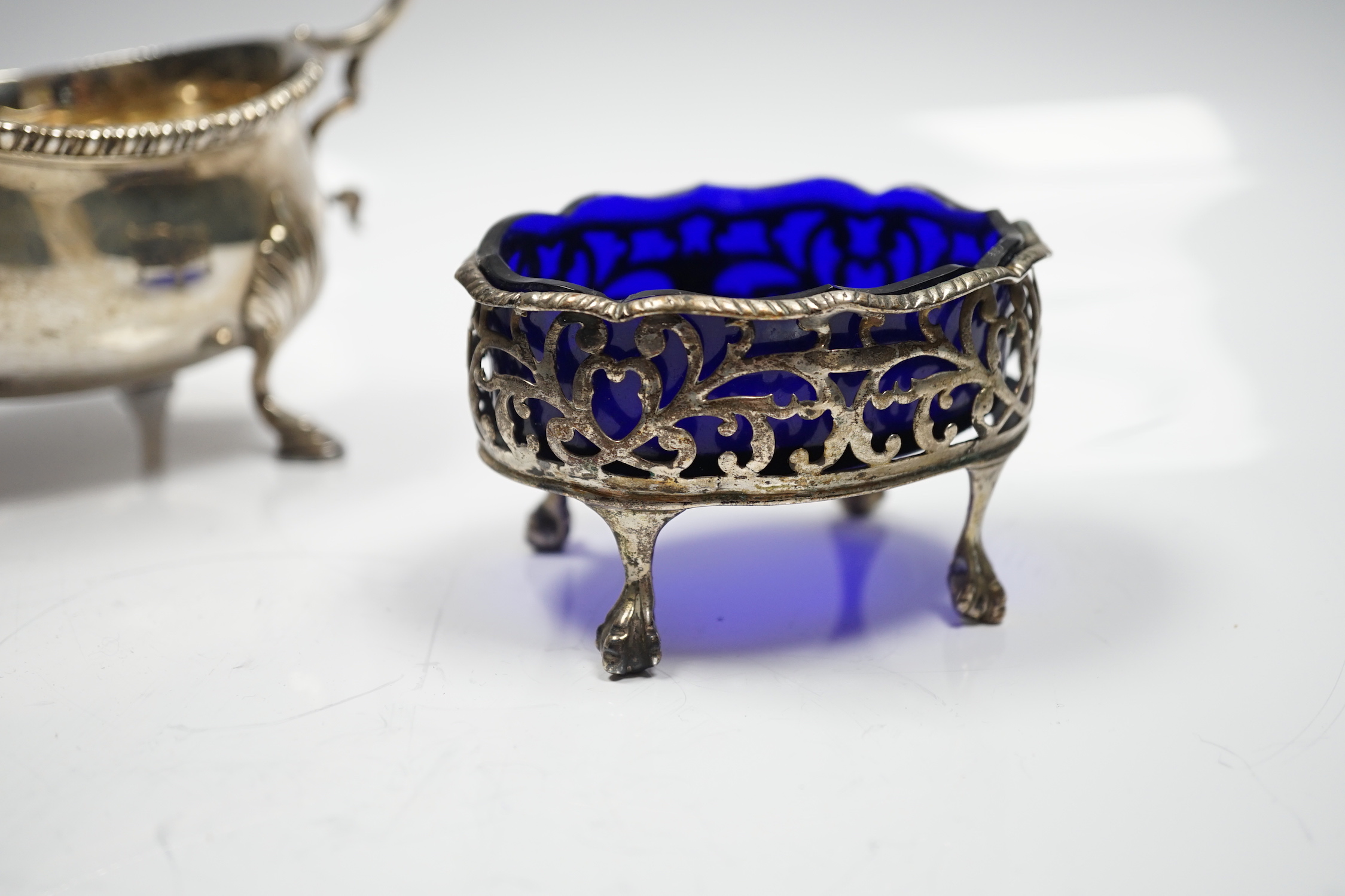 A late Victorian silver sauceboat, with flying scroll handle, William Hutton & Sons, London, 1898 and a George III pierced silver oval salt, with blue glass liner, London, 1768, 12.2oz.